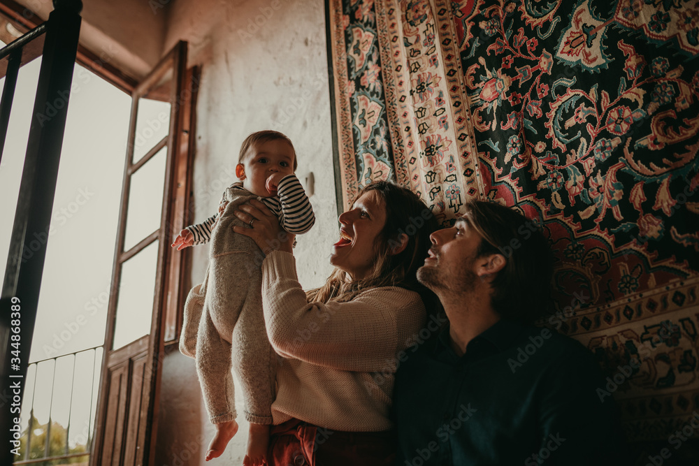 Lovely portrait of cute couple sitting inside home, on the stairs, while play with their son. Beautiful light entering through the window.