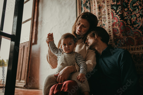 Lovely portrait of cute couple sitting inside home, on the stairs, while rest with their son. Beautiful light entering through the window.