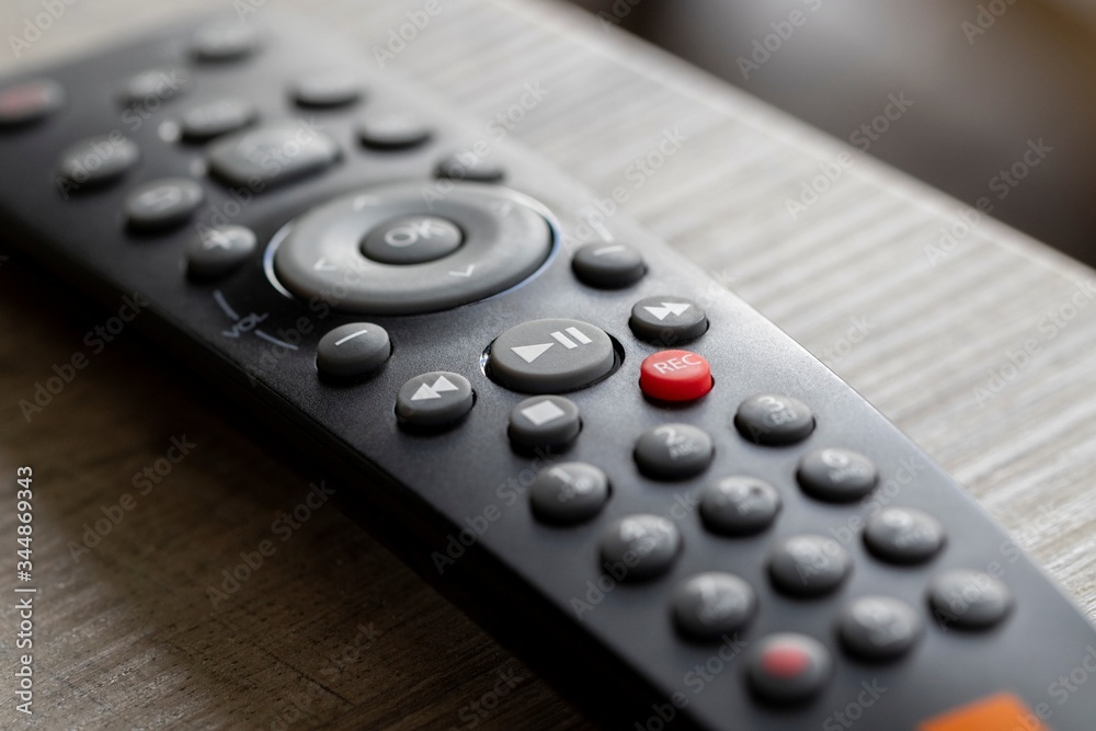A portrait of a television infrared remote control lying on a wooden table. The focus is on the play and pause button. It can also be used to control other electronic devices. A portrait of a television infrared remote control lying on a wooden table. The focus is on the play and pause button. It can also be used to control other electronic devices.
