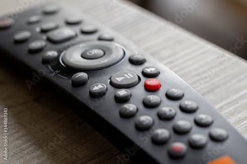 A portrait of a television infrared remote control lying on a wooden table. The focus is on the play and pause button. It can also be used to control other electronic devices.