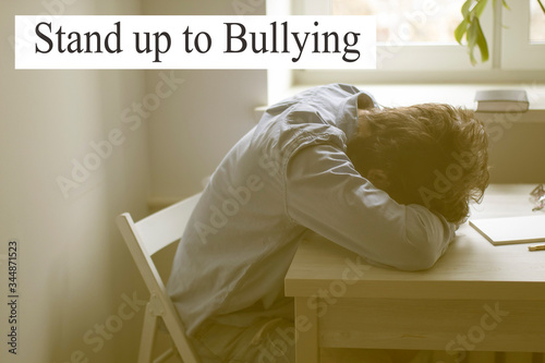 A tired man in a blue office shirt laid his head on his hands at a table opposite the window. photo