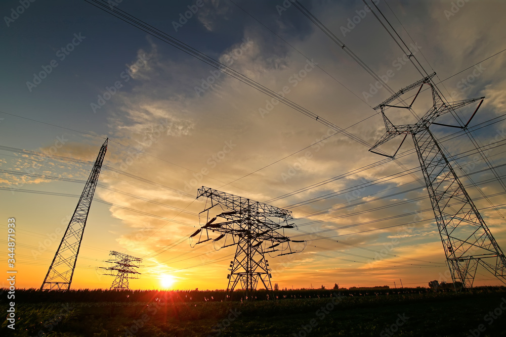 Many high voltage towers, silhouetted against the setting sun