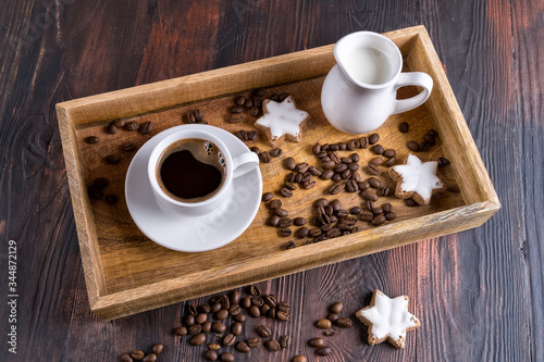 A Cup of coffee and nearby coffee beans in a wooden box on a dark wooden background.