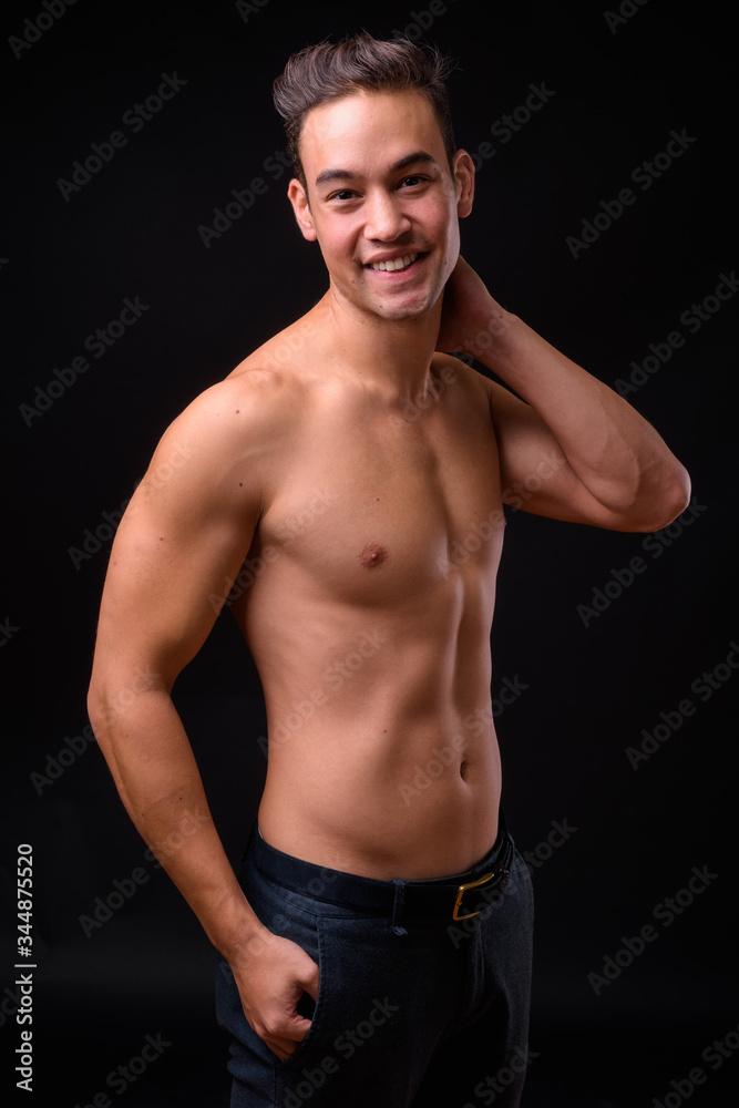 Young handsome multi ethnic man shirtless against black background