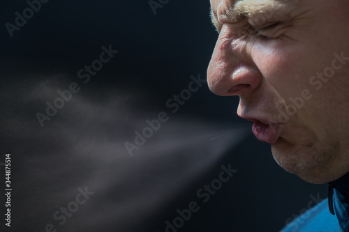 Mann niest vor schwarzem Hintergrund mit detaillierter Darstellung von ausgestoßenen Krankheitserregern
