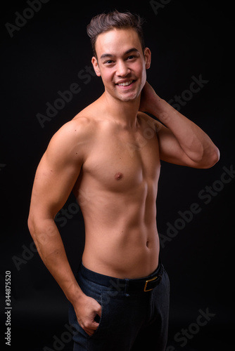 Young handsome multi ethnic man shirtless against black background
