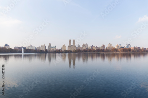 New York City skyline from one end of a Central Park lake, the water reflects the skyline and the blue sky