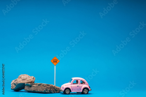 Pink car figurine next to two boulders and a construction zone sign, on blue background.