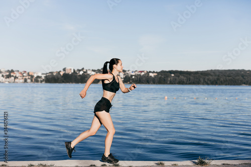 Photo of an athletic girl dressed in black during a morning jog on a city beach in the morning.