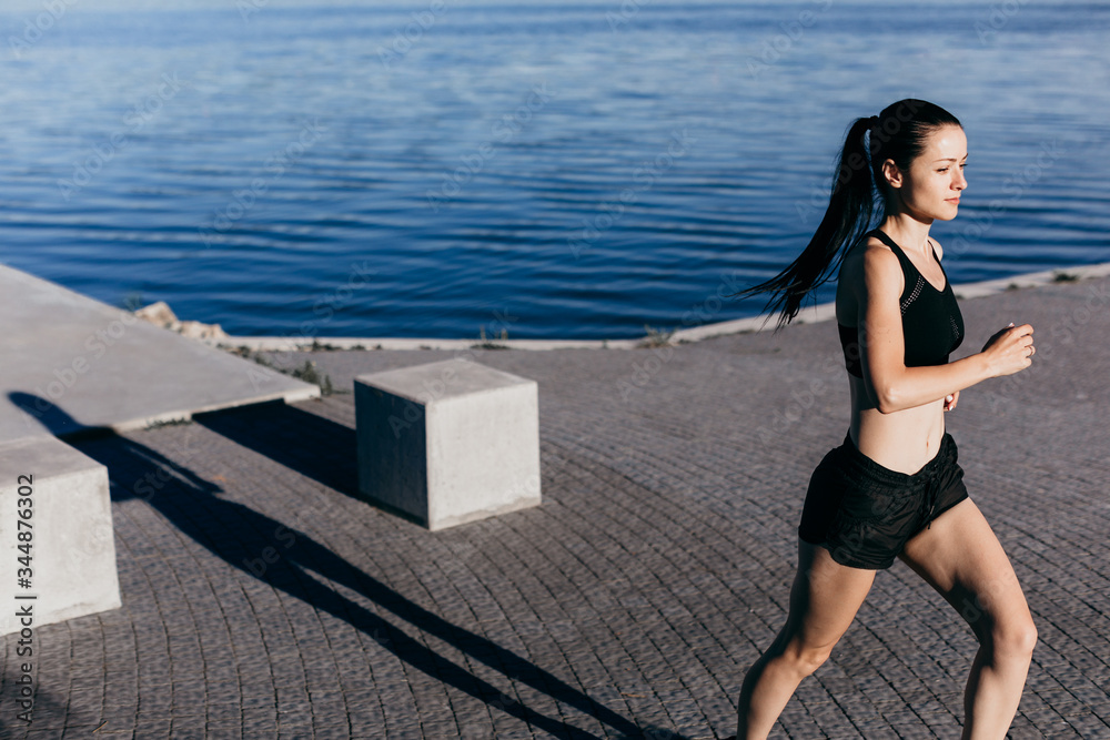 Photo of an athletic girl dressed in black during a morning jog on a city beach in the morning.