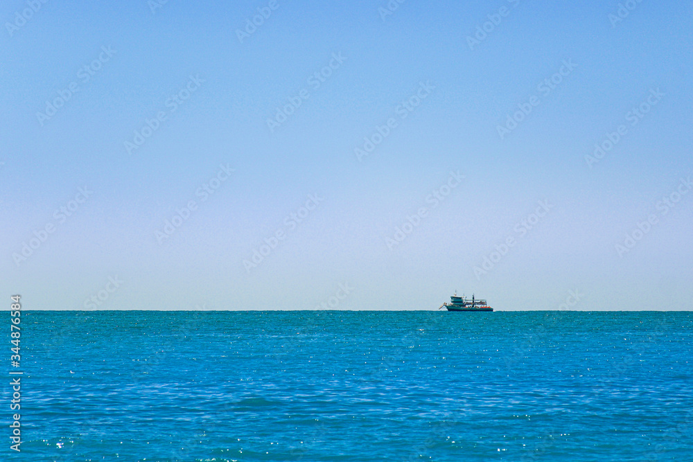 The ship sails on the horizon - blue sea and blue sky in summer.