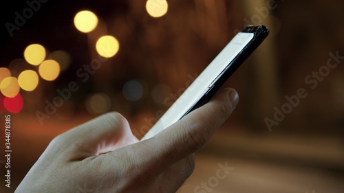 Man hands texting on a smartphone in the night city on background.Connecting and communication of social network. Blurred background and bokeh effects