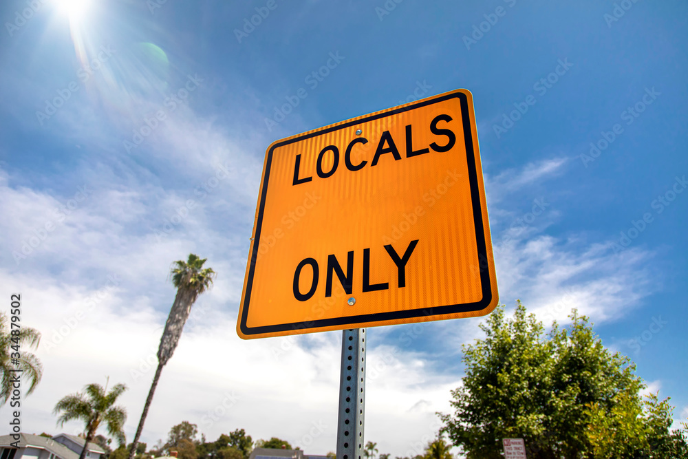 Fototapeta premium Yellow and black square road sign in neighborhood reading Local Access Only agasint a blue sky with palm trees