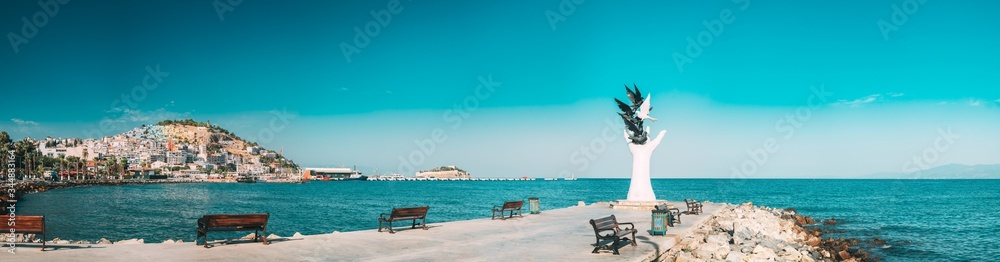 Kusadasi, Aydin Province, Turkey. Waterfront And Kusadasi Cityscape. Hand Of Peace Monument On Waterfront In Sunny Summer Day. View Of Hand Sculpture At Aegean Coast.
