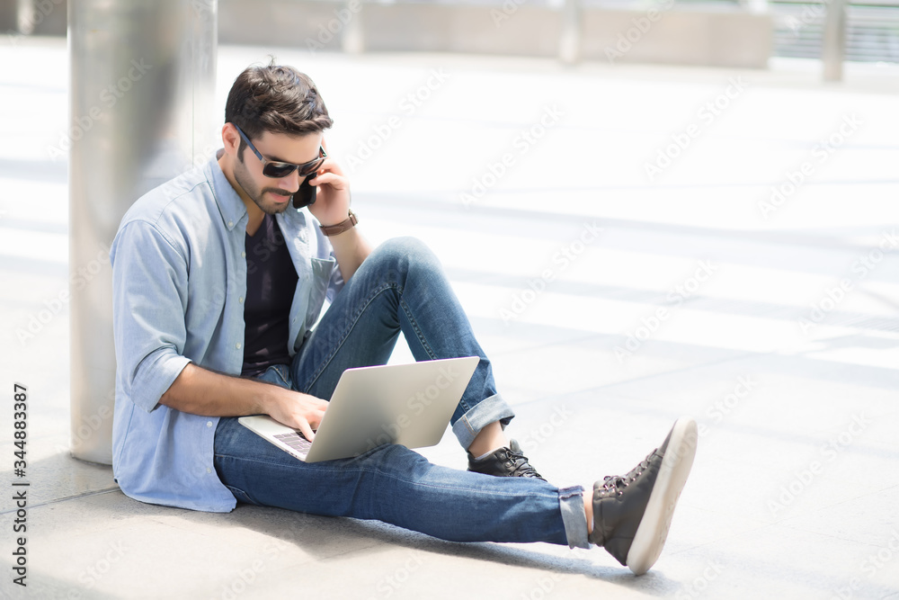 Handsome guy wearing a formal dress sitting on the phone and typing a laptop In the concept of wireless communication and online learning Handsome guy wearing a formal dress sitting on the phone and typing a laptop In the concept of wireless communication and online learning