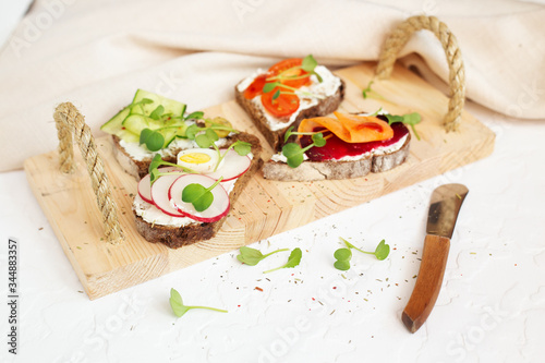 Rye bread sandwiches with cream cheese, vegetables and microgreen on wooden tray with light napkin and butter spreader. Vegetarian tapas with cucumber, tomatoes, quail eggs, radish, carrot, beet photo