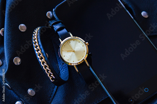 Watch with a leather strap and chains. Round dial next to a mobile phone in black and blue. Place for text. Background.