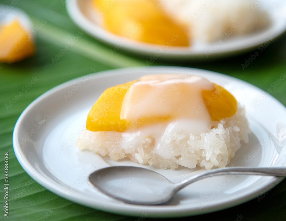 Ripe Mango with sweet sticky rice pour coconut milk in a white dish on a banana leaf. popular Thai dessert. Ripe Mango with sweet sticky rice pour coconut milk in a white dish on a banana leaf. popular Thai dessert.