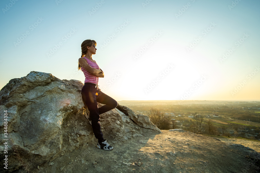 Woman hiker leaning on a big rock enjoying warm summer day. Young female climber resting during sports activity in nature. Active recreation in nature concept.