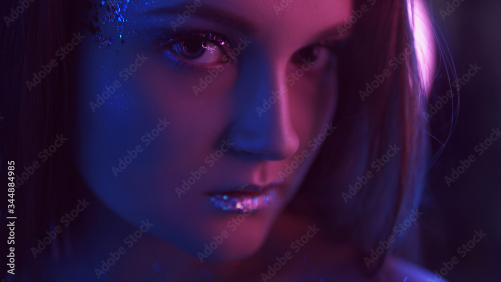 Neon girl portrait. Glamour makeup. Woman face with glitter lips in blue pink light.
