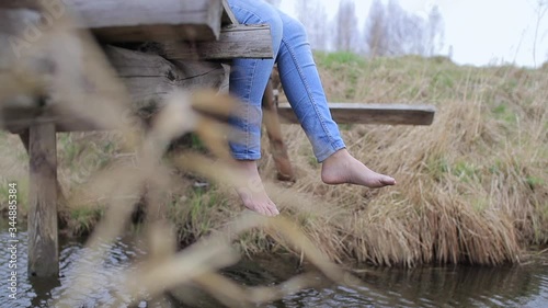 Woman legs in jeans without shoe dangling from old wooden bridge