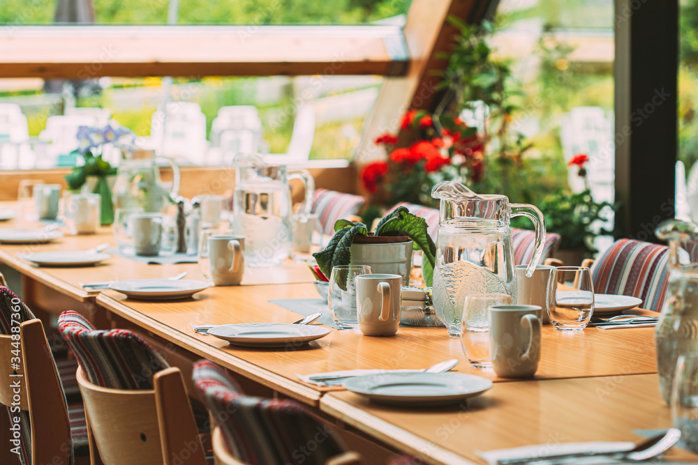 Cozy Interior Of Summer Cafe. Jug Of Water On Table And Cutlery Laid Out Cozy Interior Of Summer Cafe. Jug Of Water On Table And Cutlery Laid Out
