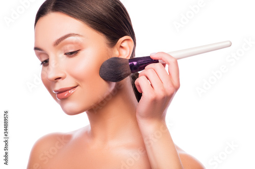 Cute smiling brunette adult girl apply make up on her fresh clean face with brush in her hand. Beauty headshot isolated on white.