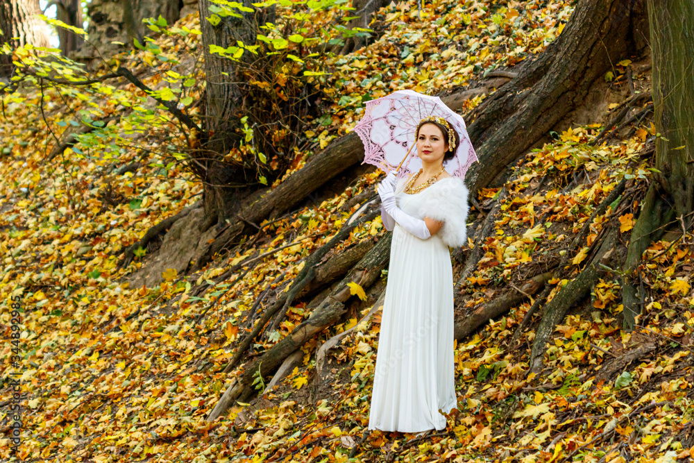 Beautiful girl in a white dress with a pink umbrella on a background of autumn trees