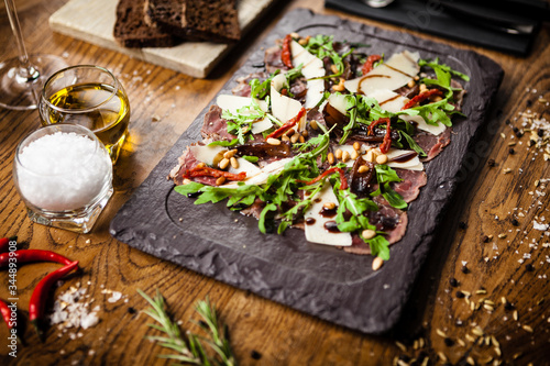 Beef carpaccio on black stone board. Delicious healthy Italian traditional antipasti snacks food closup served on a table for lunch with wine in modern gourmet restaurant.