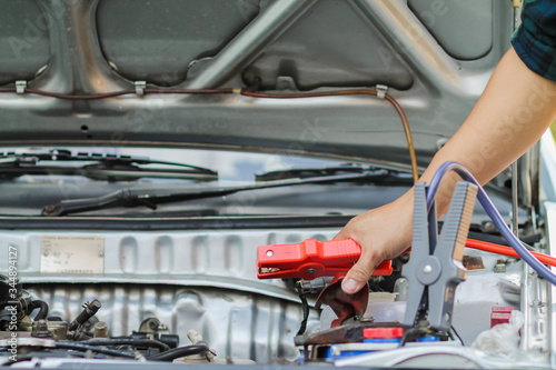 A woman holding a black and red Jumper cable that shows the positive and negative terminals to be used as a connector to stimulate the car battery to be started.Concept of car battery stimulation