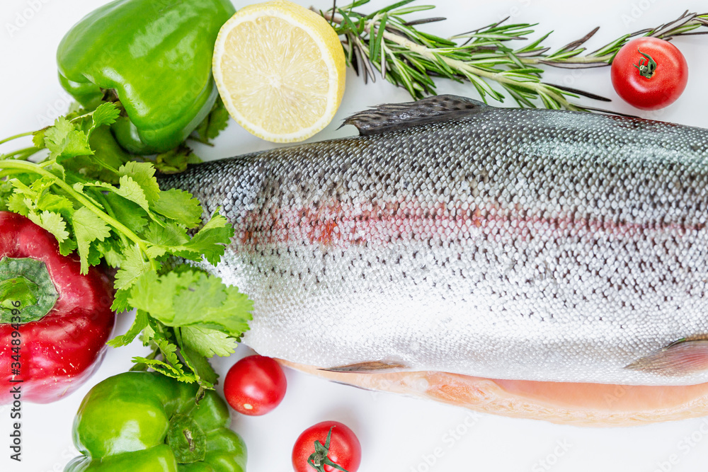 Raw sliced trout next to an assortment of red and green vegetables, lemons and rosemary. Top view.