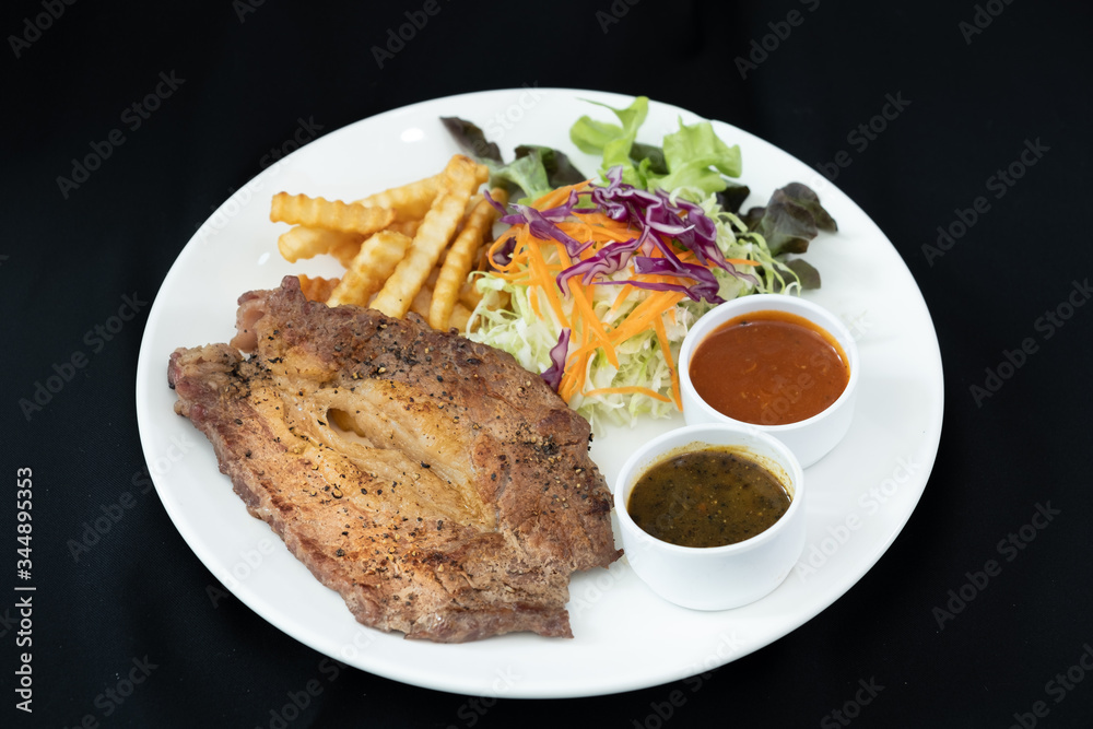 Beef steak with barbecue and paper sauces, side dish salad and french fries served on white plate, black background . Beef steak with barbecue and paper sauces, side dish salad and french fries served on white plate, black background .