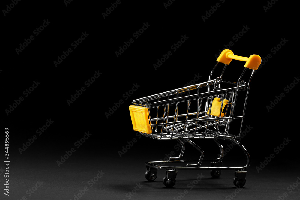 Close up of supermarket grocery push cart for shopping with yellow plastic elements on handle isolated on black background. Concept of shopping. Copy space for advertisement.