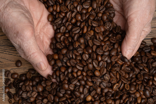 Coffee grains in hands on a wooden background. Hands of an old woman pour grain of Fresh aromatic dark coffee. Selective focus on coffee beans in hands .