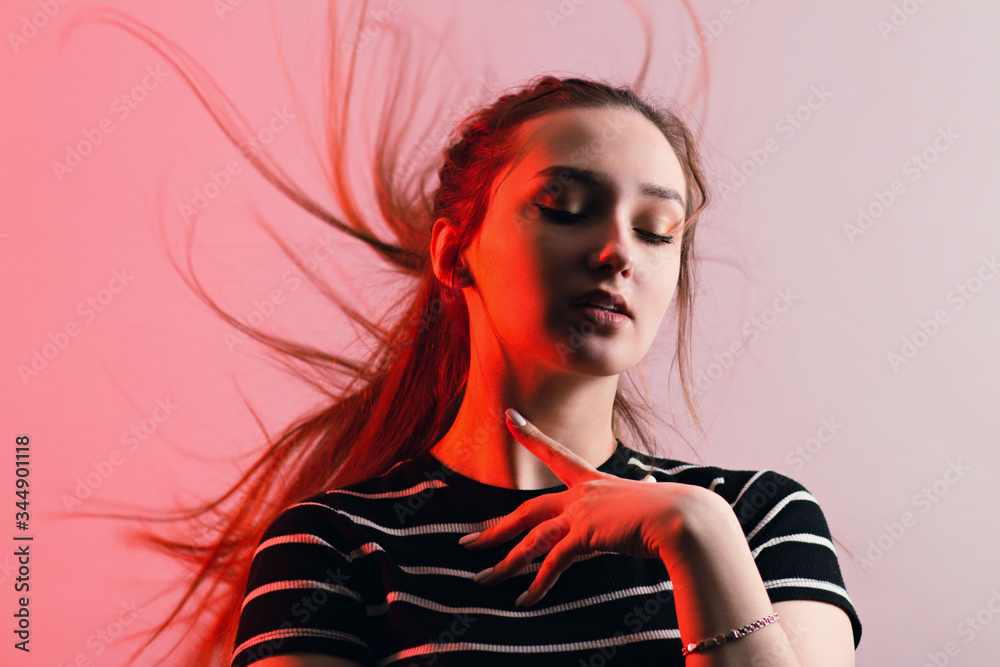 portrait of a beautiful sensual girl with makeup and with flying long hair on studio red background, concept beauty and fashion