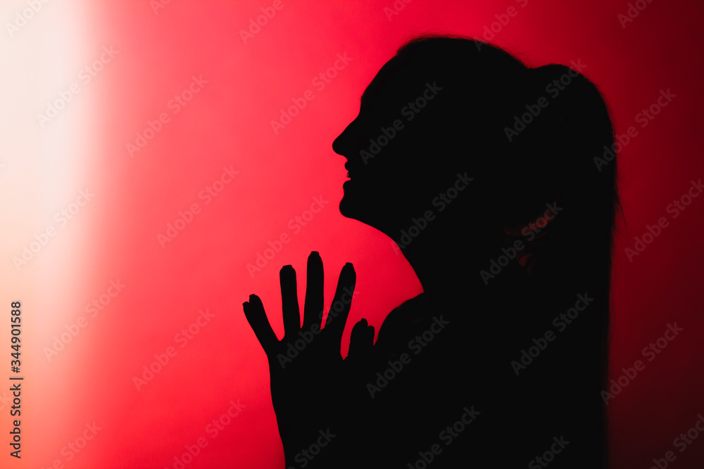 silhouette of malevolent girl on red lightened background, unrecognizable woman face profile, concept emotions