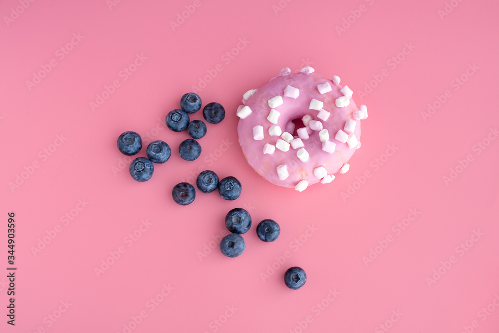 A close up of a pink donut with blueberries on pink paper background. Top view with copy space. A close up of a pink donut with blueberries on pink paper background. Top view with copy space.