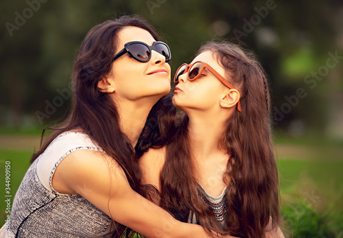 Happy fashion daughter kissing and embracing her mother in trendy sunglasses on nature summer background. Closeup
