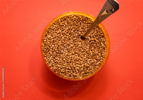 raw buckwheat in a plastic container with a spoon on a red background photo