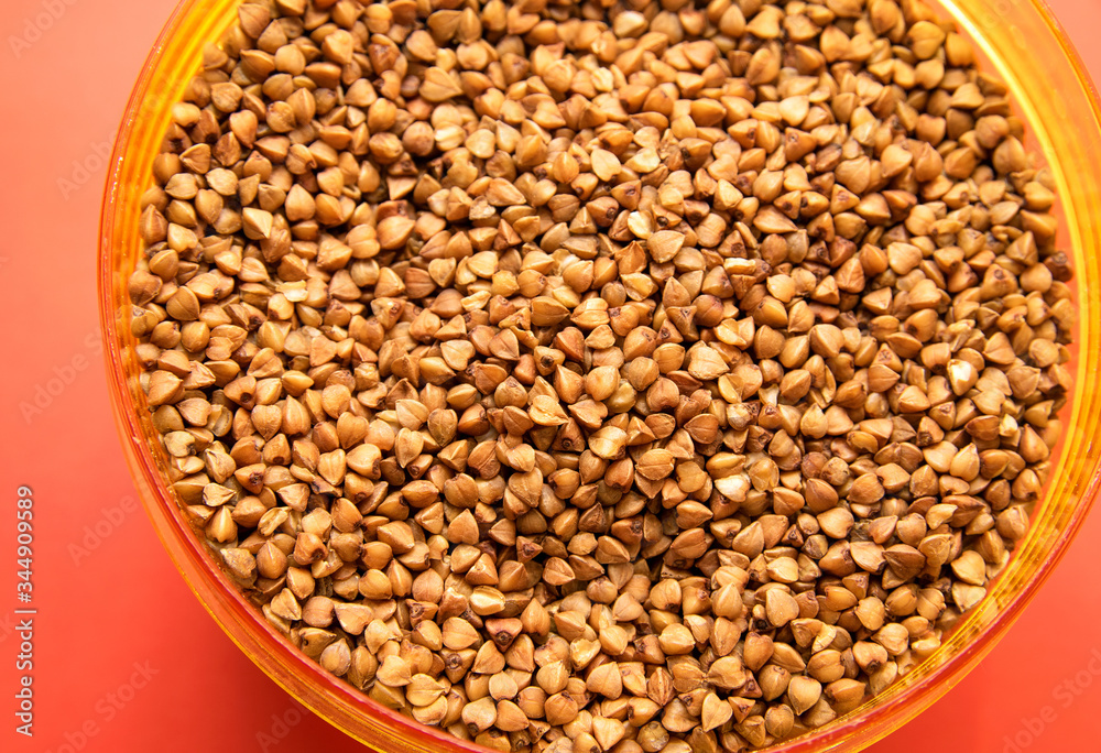 uncooked buckwheat in a plastic container on a red background