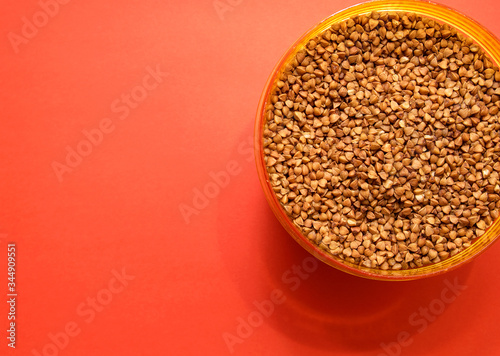 uncooked buckwheat in a plastic container on a red background photo