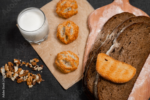 Baking, dark bread, cookies and rolls on a dark background.
Kraft paper. Milk in a transparent glass.