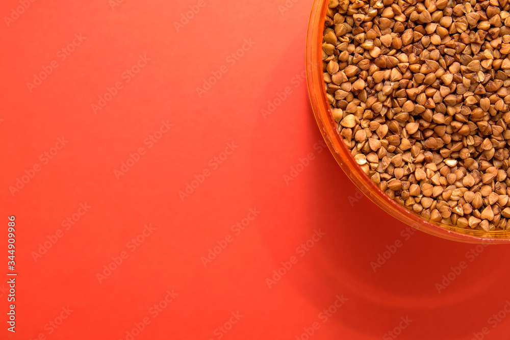 uncooked buckwheat in a container on a red background in the corner uncooked buckwheat in a container on a red background in the corner