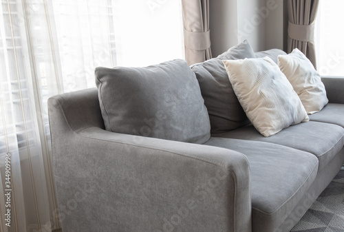 Close-up picture of grey soft with side pillows are comfortable, yet stylish and modern, for the whole family to spend their free time resting under the evening light that pass through the window.