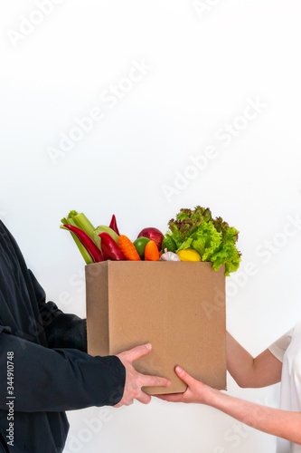 Delivery of fresh organic vegetables in a cardboard box, local market food. Male and female hands hold a box with vegetables and fruits. Vertical