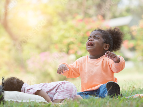 Cute little sleepy Mixed race African girl crying and throwing tantrum to mother while little brother sleeping in the park. photo