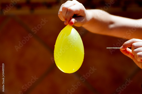 yellow balloon filled with water in a child's hand and a needle in the other hand