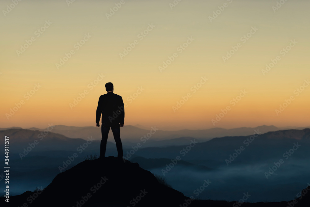 Silhouette of businessman on mountain with sunset sky background. Business success and leadership concept.