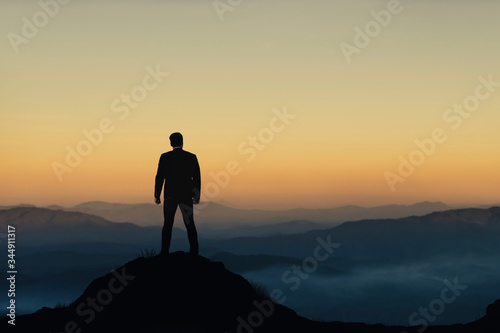 Silhouette of businessman on mountain with sunset sky background. Business success and leadership concept.