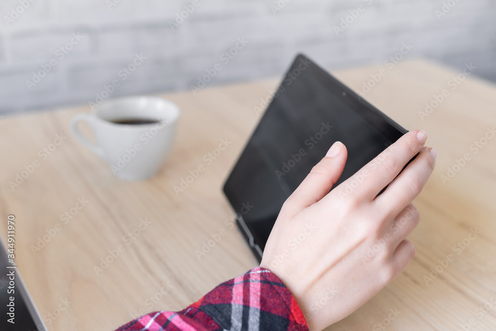 Obraz premium Woman using a tablet while sitting at a table in a cafe and drinks coffee